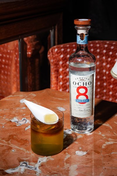 Tequila Ocho bottle with a cocktail on red marble