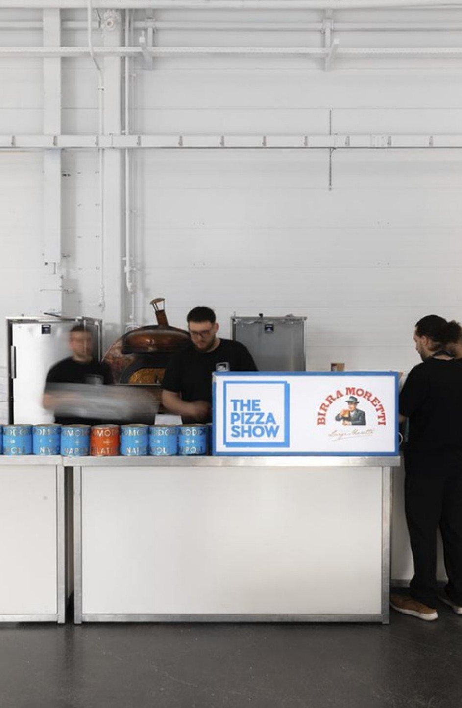 Pizza counter with branded tins in a white warehouse