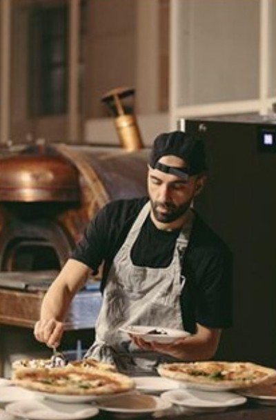 Pizzaiolo plating in front of a copper oven