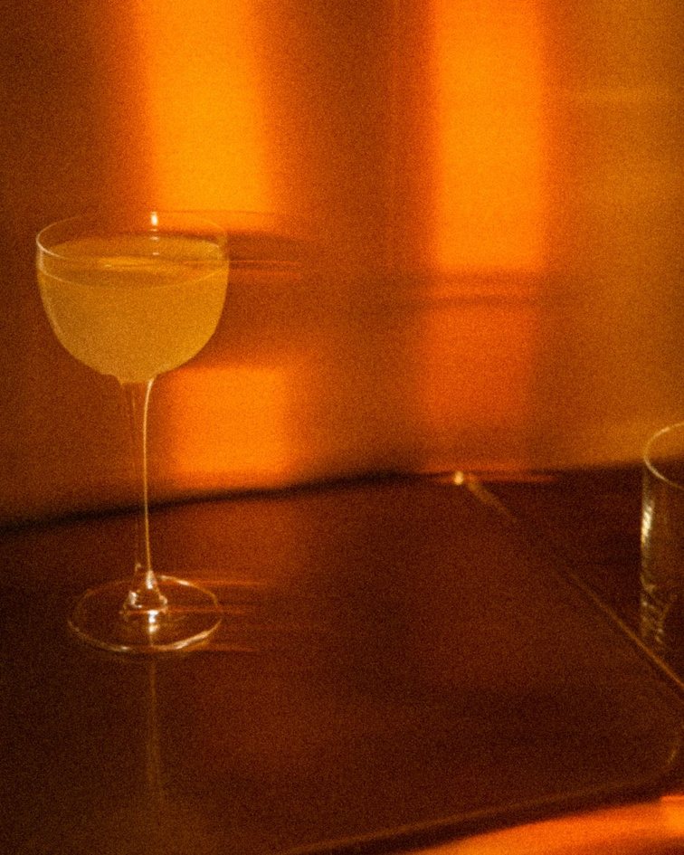A pale cocktail in a coupe glass glowing in amber evening light