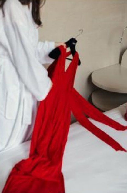 Guest in a white robe lifting a red dress from the bed