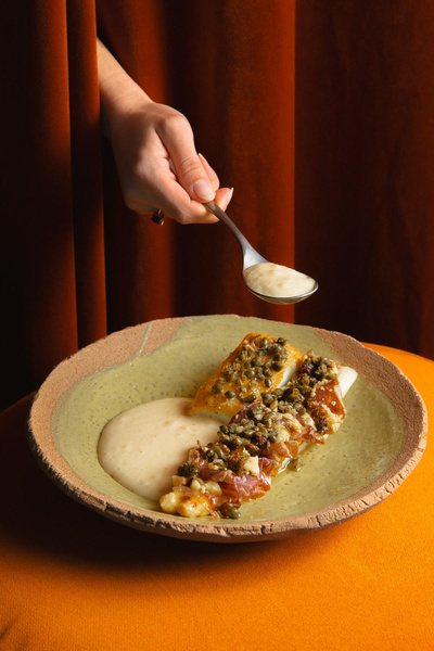 Spoon of sauce over a plated fish on orange velvet