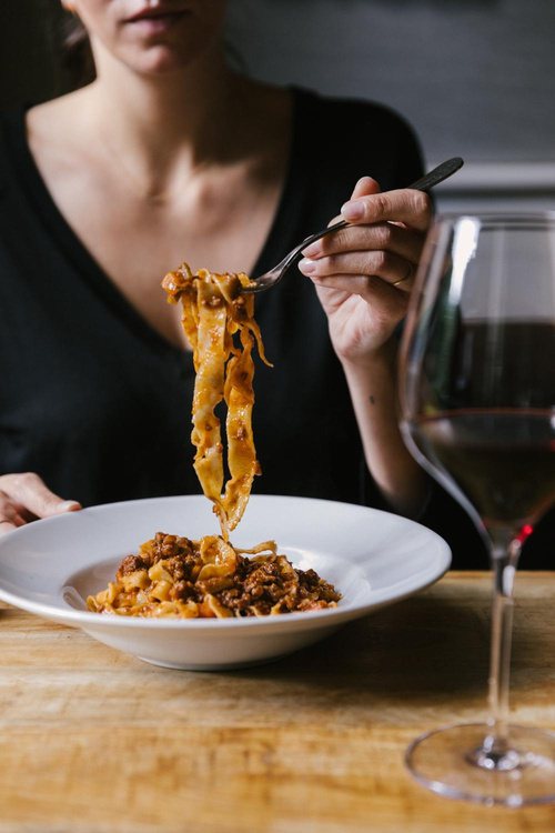Diner twirling tagliatelle with a glass of red wine