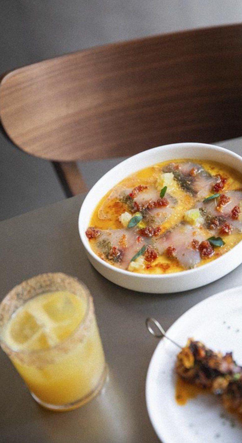 Fish crudo in a bright citrus broth next to a salted-rim cocktail