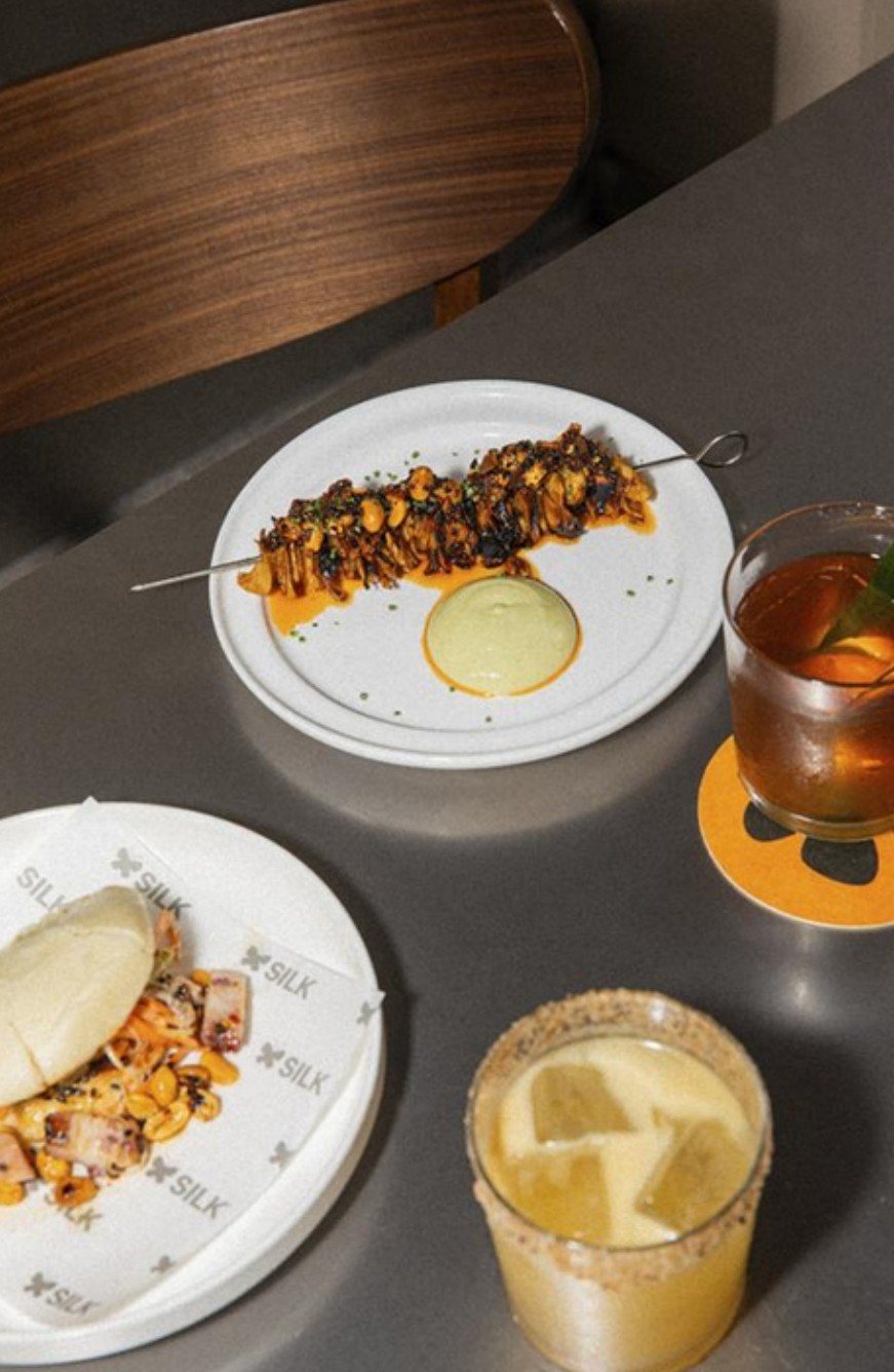 Grilled skewer, bao and cocktails on a dark table